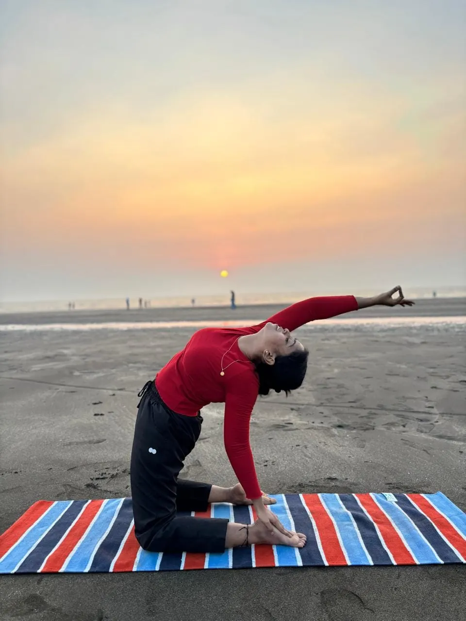 Neha in a camel pose variation on the beach at sunset