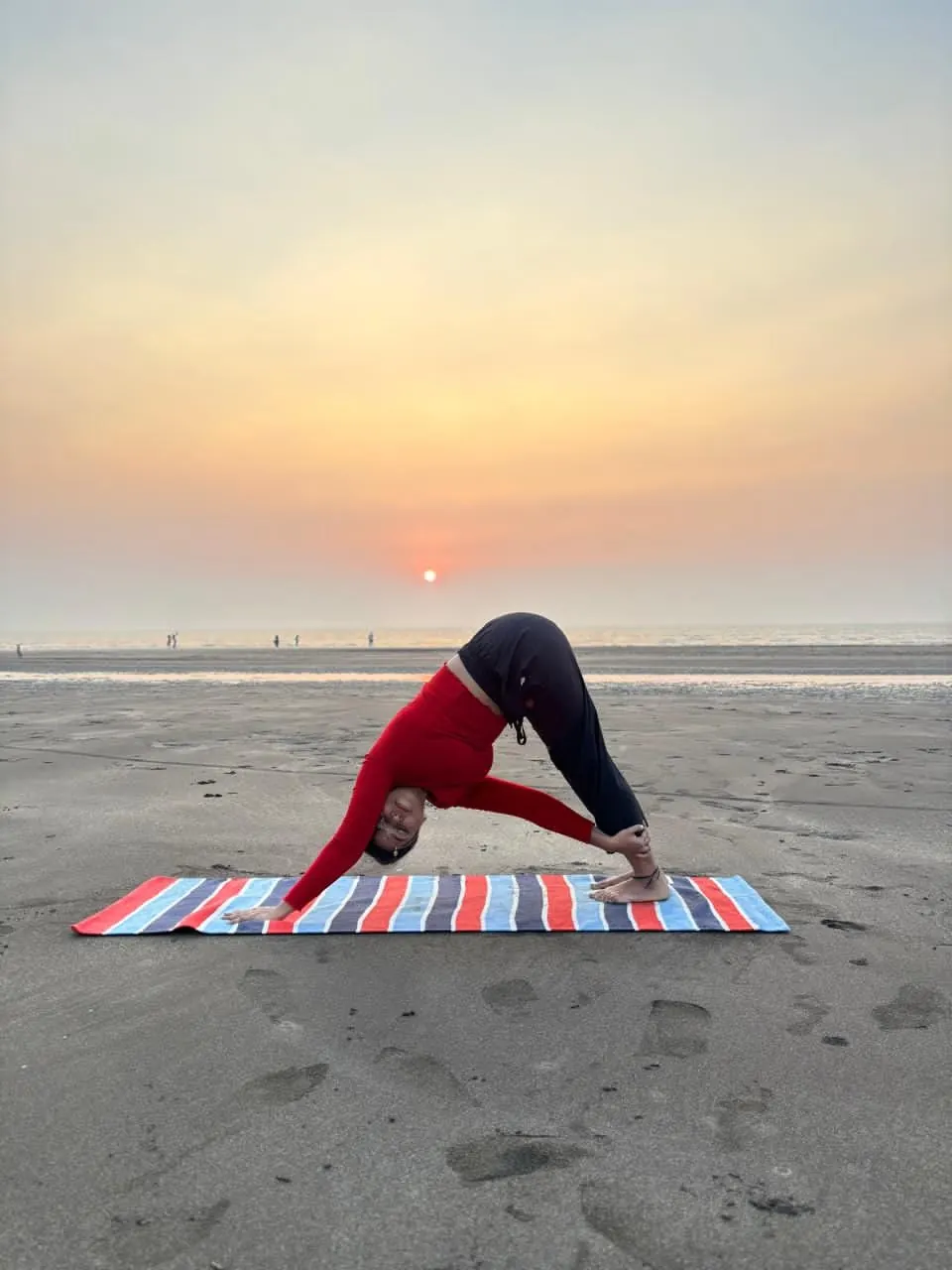 Neha in a standing forward bend on the beach at sunset