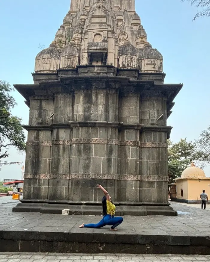 Neha in a low lunge in front of a stone temple tower