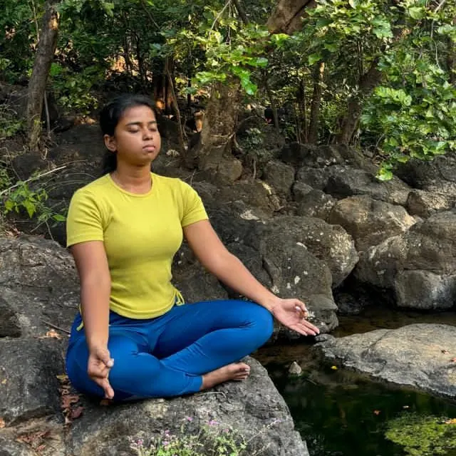 Neha meditating on a rock beside a forest stream