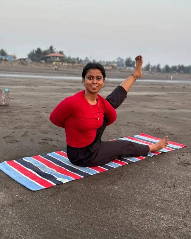 Neha smiling in a seated yoga pose on the beach