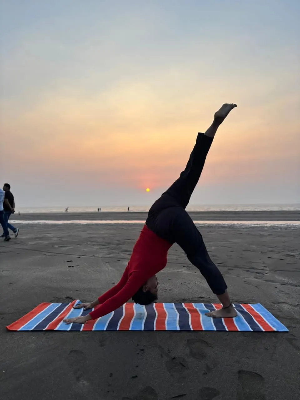 Neha in three-legged downward dog on the beach at sunset